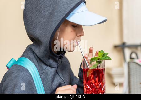 Profile Portrait Ansicht von niedlichen Preteen kleines Kind Mädchen in grau Hoodie genießen drinkong gesunde Beerenlimonade Saft Kompott Cocktail zu Fuß im Freien Stockfoto