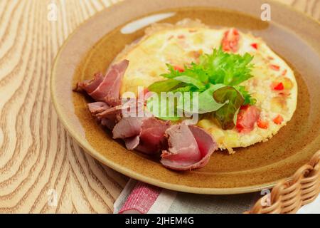 Leckeres Frühstück. Gebratenes Omelette mit in Scheiben geschnittenem Schinken aus nächster Nähe Stockfoto