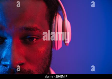 Junger schwarzer Mann, der Musik hört, mit Kopfhörern, die über einer violetten Wand isoliert sind Stockfoto