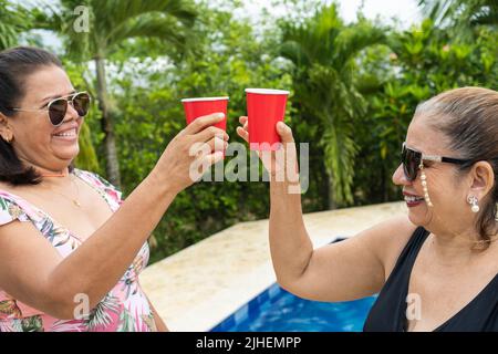 Zwei ältere Damen, die an einem Sommertag mit einem Getränk toasten. Stockfoto