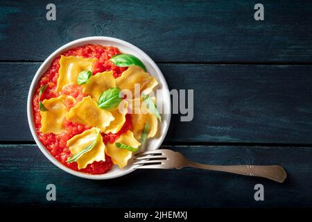 Ein Teller mit Ravioli mit Tomatensauce und Basilikum, italienisches Gericht, von oben auf einem dunklen Holzhintergrund mit einem Platz für Text geschossen Stockfoto