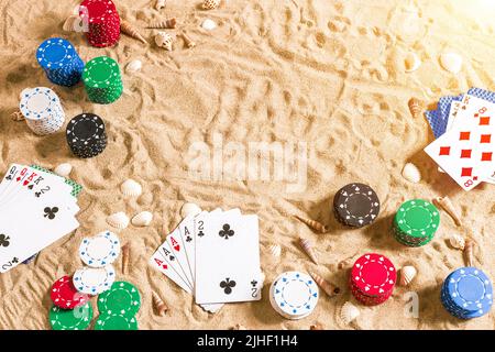 Beachpoker. Chips und Karten auf dem Sand mit Muscheln. Draufsicht. Speicherplatz kopieren. Flach liegend. Beachpoker. Chips und Karten auf dem Sand mit Muscheln. Oben vi Stockfoto