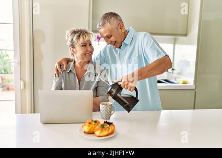 Ein älteres kaukasisches Paar, das mit einem Laptop in der Küche frühstückte. Stockfoto