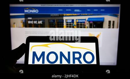 Person, die das Smartphone mit dem Logo des US-amerikanischen Automobildienstleisters Monro Inc. Auf dem Bildschirm vor der Website hält. Konzentrieren Sie sich auf die Telefonanzeige. Stockfoto