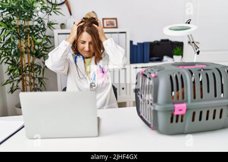 Mittlere Alter Tierarzt Frau, die in PET-Klinik leiden unter Kopfschmerzen verzweifelt und gestresst, weil Schmerzen und Migräne. Hände auf dem Kopf. Stockfoto