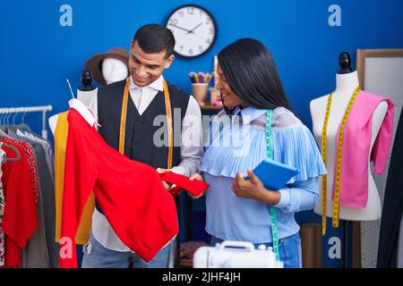Mann und Frau Schneiderinnen halten Touchpad und T-Shirt im Nähstudio Stockfoto