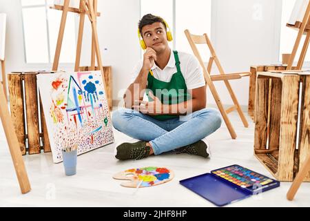 Junger hispanischer Mann im Kunststudio mit Hand auf Kinn, der über Fragen nachdenkt, nachdenklichen Ausdruck. Lächelnd mit nachdenklichen Gesicht. Zweifelskonzept. Stockfoto