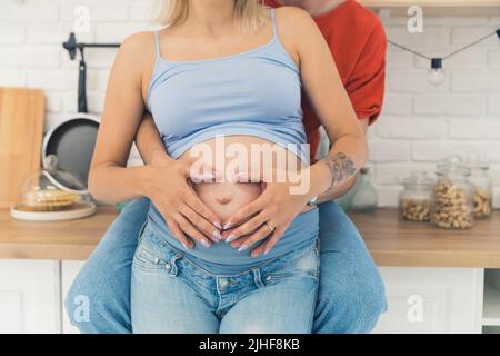 Unverkennbares Paar in der Küche. Partner halten ihre Hände zusammen auf dem schwanger Bauch. Schwangerschaft und Zweisamkeit. Hochwertige Fotos Stockfoto