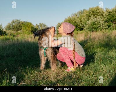 Kleines Mädchen umarmt spielen mit Hund im Freien. Familienspaziergängen Spaß haben Zeit zusammen in der Natur zu verbringen. Kind mit Haustier Freund auf Sommerwiese. Acti Stockfoto