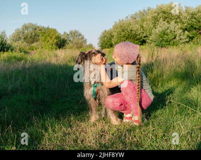 Kleines Mädchen umarmt spielen mit Hund im Freien. Familienspaziergängen Spaß haben Zeit zusammen in der Natur zu verbringen. Kind mit Haustier Freund auf Sommerwiese. Acti Stockfoto