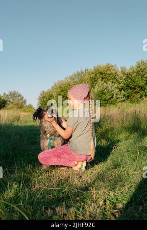 Kleines Mädchen umarmt spielen mit Hund im Freien. Familienspaziergängen Spaß haben Zeit zusammen in der Natur zu verbringen. Kind mit Haustier Freund auf Sommerwiese. Acti Stockfoto