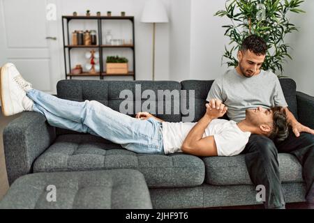 Zwei hispanische Männer, die zu Hause lächeln und selbstbewusst auf dem Sofa sitzen Stockfoto