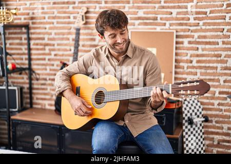 Junger Musiker, der im Musikstudio lächelnd und selbstbewusst klassische Gitarre spielt Stockfoto