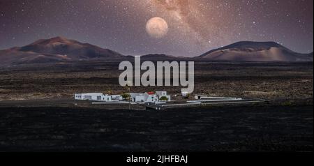 Atemberaubende nächtliche Panoramalandschaft mit Vulkankrater im Timanfaya Nationalpark. Vollmond über La Gueria, Lanzarote, Kanarische Inseln, Spanien Stockfoto