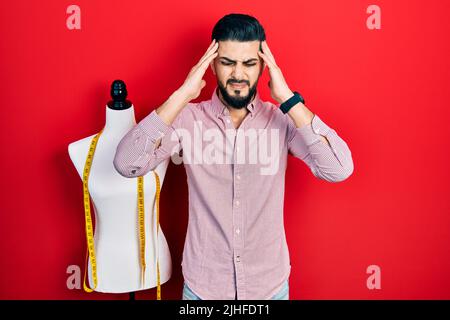 Schöner Schneider Mann mit Bart stehen bei Übungspuppe mit Hand auf dem Kopf, Kopfschmerzen, weil Stress. Leiden Migräne. Stockfoto