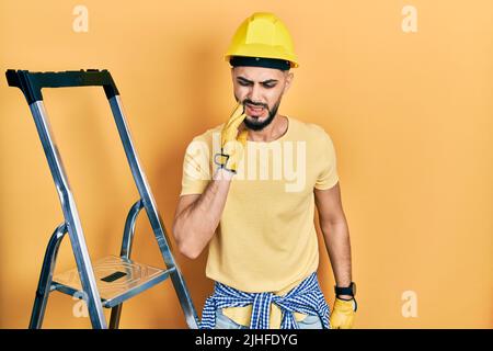 Schöner Mann mit Bart durch Bautreppe trägt Hardhut berühren Mund mit Hand mit schmerzhaften Ausdruck wegen Zahnschmerzen oder Zahnerkrankungen Stockfoto
