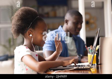 Bild von afroamerikanischem Vater und Tochter, die online Unterricht haben und zusammenarbeiten Stockfoto