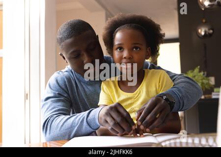 Bild eines glücklichen afroamerikanischen Vaters und einer Tochter mit Sehbehinderung beim Lesen in Blindenschrift Stockfoto