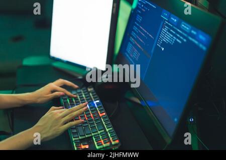 Unerkannte junge Frau, die in einem Gamer-Sessel sitzt und auf einer hintergrundbeleuchteten Tastatur tippt. Hacking-Konzept. Hochwertige Fotos Stockfoto