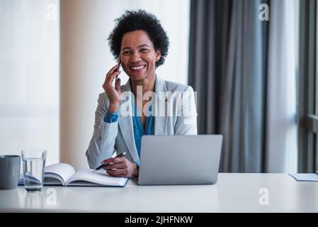 Nahaufnahme einer Geschäftsfrau, die auf einem Smartphone spricht. Glückliche weibliche Geschäftsführerin trägt formelle Kleidung. Sie arbeitet in einem Unternehmensbüro. Stockfoto