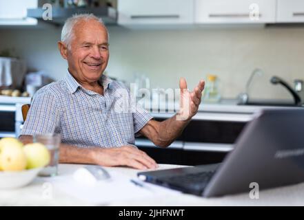 Alter Mann mit Laptop, der durch Videoanruf spricht Stockfoto