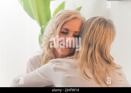 Eine unkenntliche kaukasische Frau mit glattem blondem Haar umarmt eine elegante Dame mittleren Alters mit welligen Haaren. Supportkonzept. Hochwertige Fotos Stockfoto