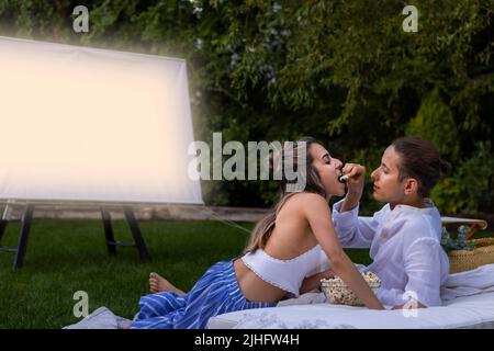 Ein junges heterosexuelles Paar, das im Gartenkino romantische Popcorne als Zeichen der Liebe isst Stockfoto