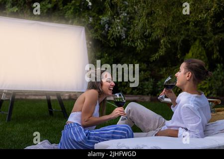 Verliebt lachen und Spaß haben, während sie Rotwein trinken und einen Film als Date ansehen Stockfoto