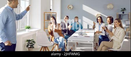 Die Leute applaudieren ihrem Kollegen, der vor ihnen steht, und haben Spaß daran, Geschäftspräsentation zu machen. Stockfoto