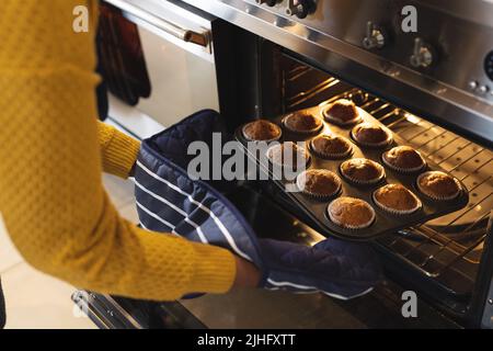 Bild des mittleren Abschnitts einer afroamerikanischen älteren Frau, die Cupcakes aus dem Ofen herausnahm Stockfoto