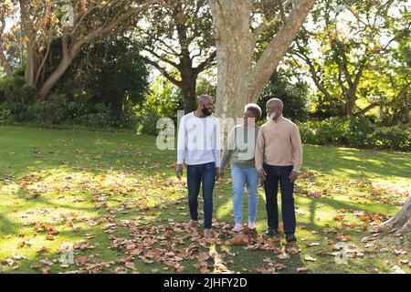 Bild von glücklichen afroamerikanischen Eltern und erwachsenem Sohn, der im Garten spazieren geht Stockfoto