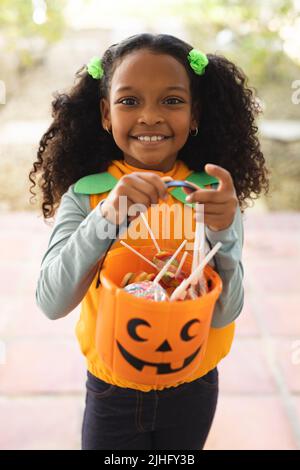 Vertikales Bild von glücklichen afroamerikanischen Mädchen in halloween-Kostüm mit Korb Stockfoto