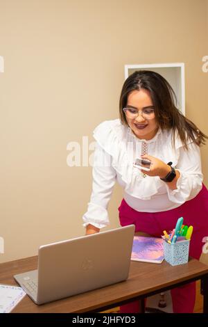 Die vertikale Ansicht einer Frau, die ihr Smartphone hält, während sie am Schreibtisch steht Stockfoto