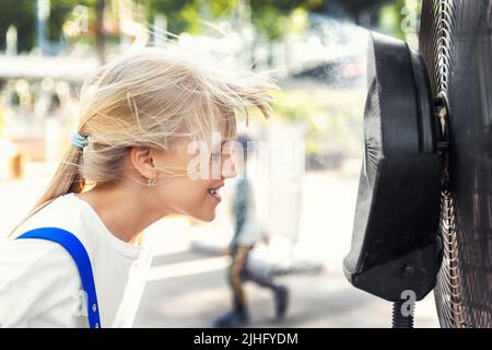 Profil Seite Nahaufnahme Ansicht niedlichen kleinen blonden Mädchen genießen frische, mit Feuchtigkeit befeuchtete Luft weht aus großen Kühlventilator Maschine heißen sonnigen Sommerwetter Stockfoto