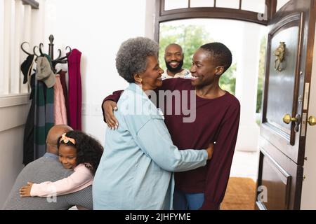 Bild einer glücklichen, mehrgenerationenigen afroamerikanischen Familie, die das Haus betreten und sich gegenseitig willkommen heißen Stockfoto