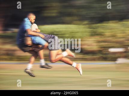 Mixed Race Rugby-Spieler, der versucht, einen Gegner während eines Rugby-Spiels draußen auf dem Spielfeld anzugreifen. Junger hispanischer Mann, der einen Gegner in einem Angriff Stockfoto