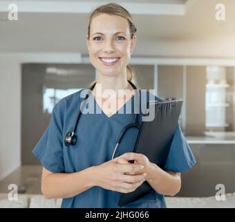 Ein schöner junger Arzt, der glücklich und freundlich bei der Arbeit wartet. Lächelnder kaukasischer Mitarbeiter im Gesundheitswesen, der ein Stethoskop trägt und ein hält Stockfoto