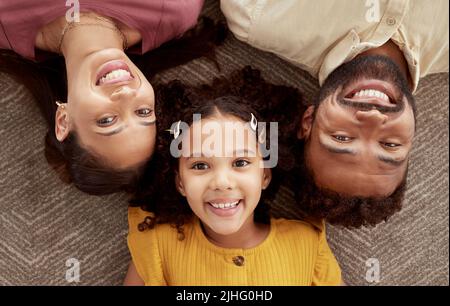 Oben Porträt von gemischten Rennen Eltern genießen Wochenende mit Tochter im Wohnzimmer zu Hause. Lächelndes hispanische Mädchen umarmte Mutter und Vater und bonding Stockfoto