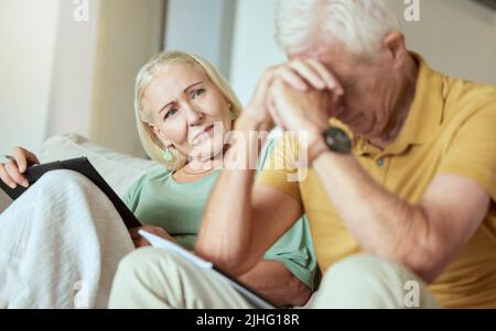 Unglückliches älteres Paar, das zusammen auf einem Sofa sitzt und gestresst aussieht. Ältere kaukasische Männer und Frauen, die sich während ihrer Zeit Sorgen um ihre Zukunft machen Stockfoto