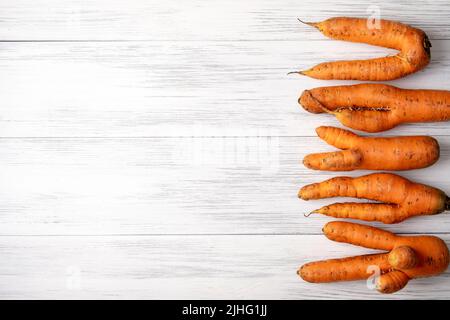 Hässliche Karotten liegen auf einer hellen Holzoberfläche Stockfoto