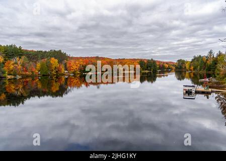Wunderschöner See, umgeben von einem Wald auf dem Gipfel der Herbstfärbung an einem bewölkten Herbsttag. Die Leute im Kanu sind mitten im See. Stockfoto
