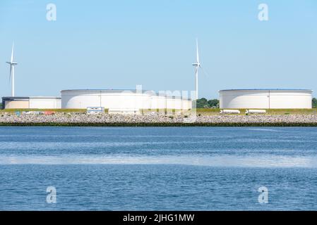 Große Öltanks in einem Hafen an einem sonnigen Sommertag. Windturbinen sind im Hintergrund. Stockfoto