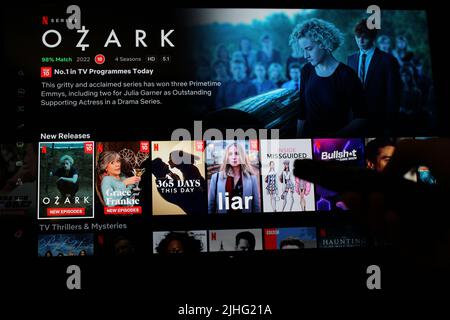 London, Großbritannien: 1. Mai 2022: Netflix-App auf dem fernsehbildschirm, die die Show Ozark mit dem Schatten einer Person zeigt, die eine TV-Fernbedienung vor sich hält. Stockfoto