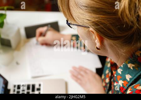 Defokussieren weiblicher Hand Schreibfeder. Unkenntlich elegante Frau, die im Büro am Computer arbeitet. Beginn oder Ende eines Arbeitstages. Arbeitsbereich. Papierkram. Zeit Stockfoto