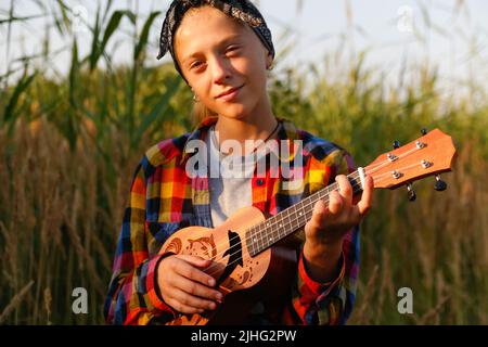 Defokussieren Mädchen mit Gitarre. Teen Mädchen zu Fuß auf Natur Hintergrund. Kleines Mädchen draußen auf grüner Wiese. Generation z. Sommerzeit. Menschen, Musiker Stockfoto