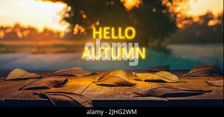Heruntergefallene Blätter auf einem Holztisch mit Neonlicht-Text. Hallo Herbstkonzept Stockfoto