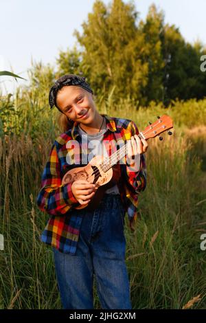 Defokussieren Mädchen mit Gitarre. Teen Mädchen zu Fuß auf Natur Hintergrund. Kleines Mädchen draußen auf grüner Wiese. Generation z. Herbst. Menschen, Musiker Stockfoto