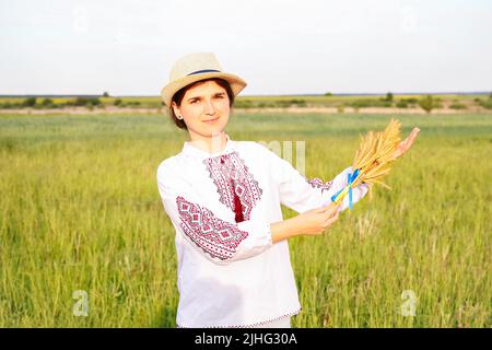 Unschärfe junge Frau in vyshywanka und Hut hält Bouquet von reifen goldenen Dornen von Weizen gebunden und Flagge auf der Wiese Natur Hintergrund. Alarmmeldung Stockfoto