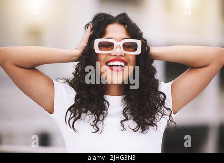 Schöne Mixed-Race-Mode Frau trägt Sonnenbrille, während draußen stehen. Junge hispanische Frau, die stilvoll und trendy, lächelnd und glücklich aussieht Stockfoto