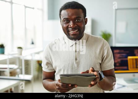 Porträt eines afrikanischen IT-Spezialisten, der die Kamera anlächelt, während er im Büro auf einem digitalen Tablet steht Stockfoto